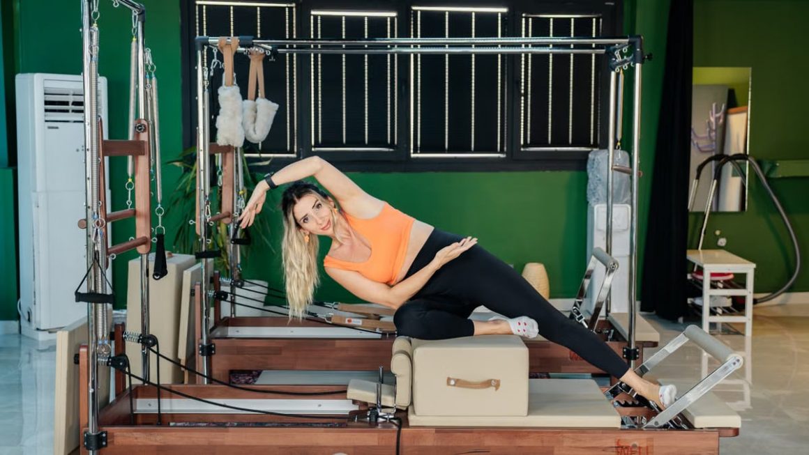 Woman performing side stretch exercise on Pilates reformer machine indoors.